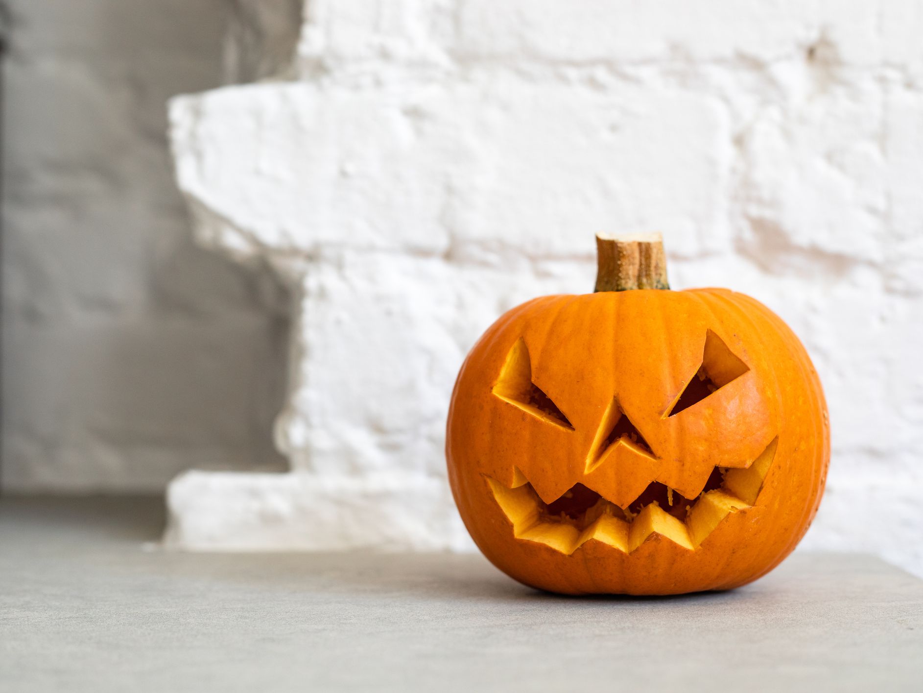 halloween-pumpkin-lantern-in-front-of-a-white-brick-wall-1174885259-9f6db00eec6e4044b0fe654858d5cdc7